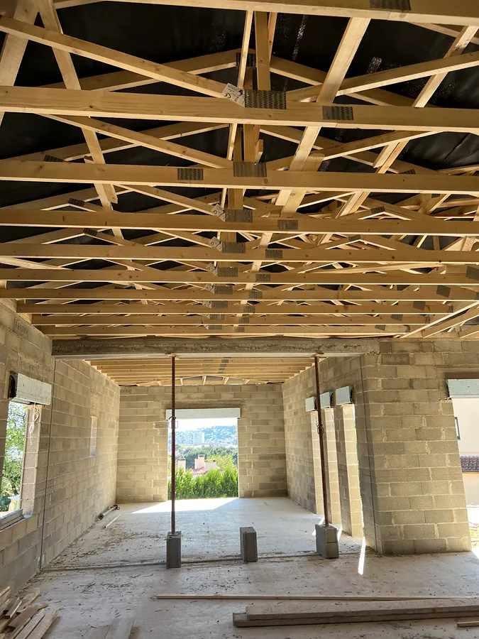 Intérieur de la maison en blocs béton sous une charpente en fermettes bois