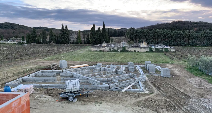 Fondations et premiers rangs de blocs d’une maison à Sazé, vignes et collines en arrière-plan