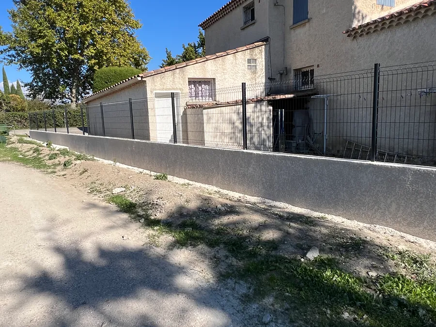 Mur bahut enduit au pied d’une clôture grillagée
