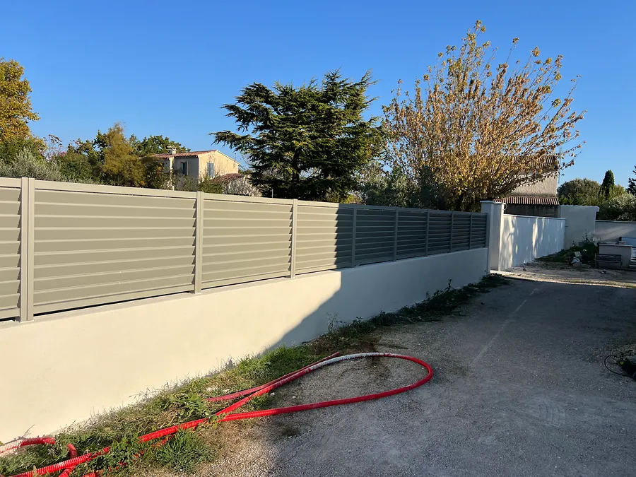 Mur bahut enduit surmonté de panneaux de clôture le long d’une allée