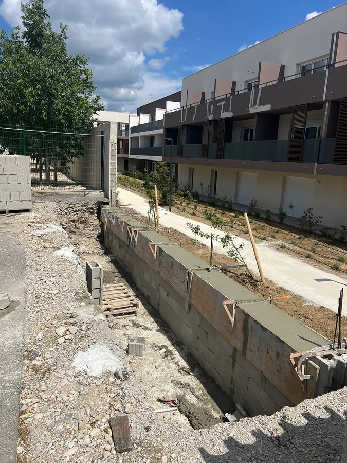 Fondation et premiers rangs de blocs béton du nouveau mur, le long d’une résidence