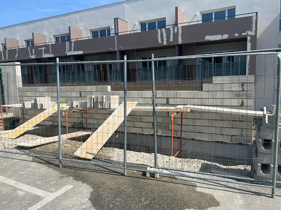 Mur en blocs béton en cours d’élévation derrière les barrières de chantier
